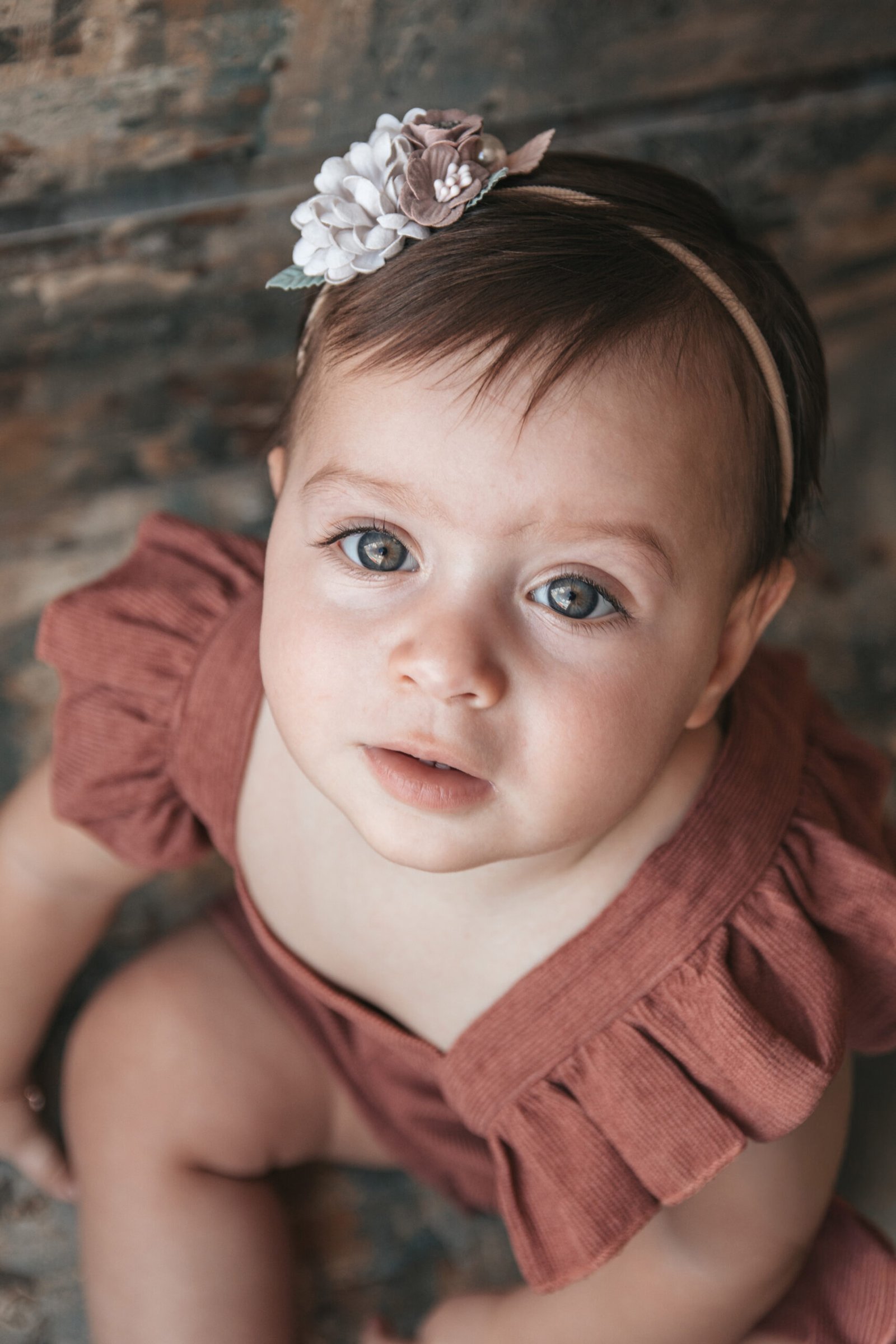 Bebê com vestido marrom e tiara de flores